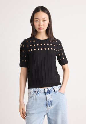 Svart strikket topp med korte ermer som har et åpent hullmønster, ribbet tekstur og en tettsittende silhuett; båret med lyseblå denimjeans.