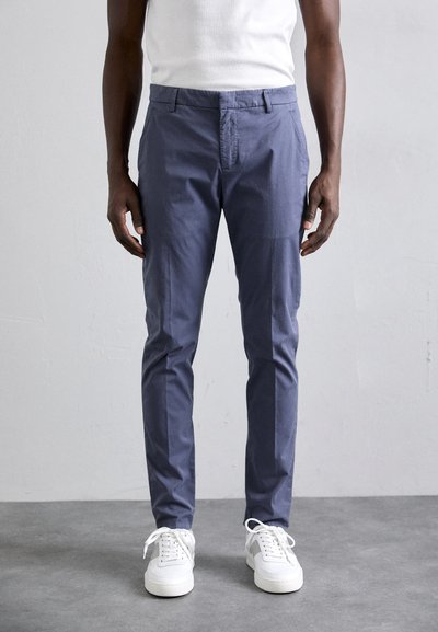 Pantalons tapered bleu marine en tissu léger, avec une taille plate, passants de ceinture, poches latérales, et associés à des baskets blanches.