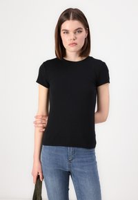 Tricou negru cu mânecă scurtă, realizat dintr-un material neted și elastic, cu guler rotund și un design ajustat, asortat cu blugi din denim albastru.