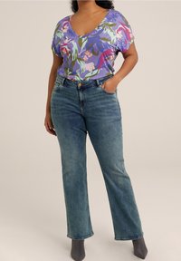 Krátký rukáv, fialový květinový top s výstřihem do V, v kombinaci s modrými džíny rovného střihu. Významné detaily zahrnují přední knoflík a kapsy.