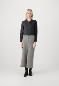 Czarna krótka kurtka z dwoma przednimi kieszeniami, zestawiona z szaro-denimową maxi spódnicą z rozcięciem z przodu. Czarne botki za kostkę dopełniają outfit.