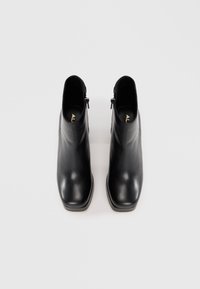 Black leather ankle boots with a smooth finish, square toe, and a side zipper. Flat soles with minimal texture. Gold logo visible inside.