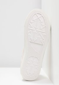 Růžová teniska s texturovaným textilním svrškem a bílou gumovou podrážkou. Na podrážce je geometrický hvězdicový vzor. Úhlový pohled na podrážku.