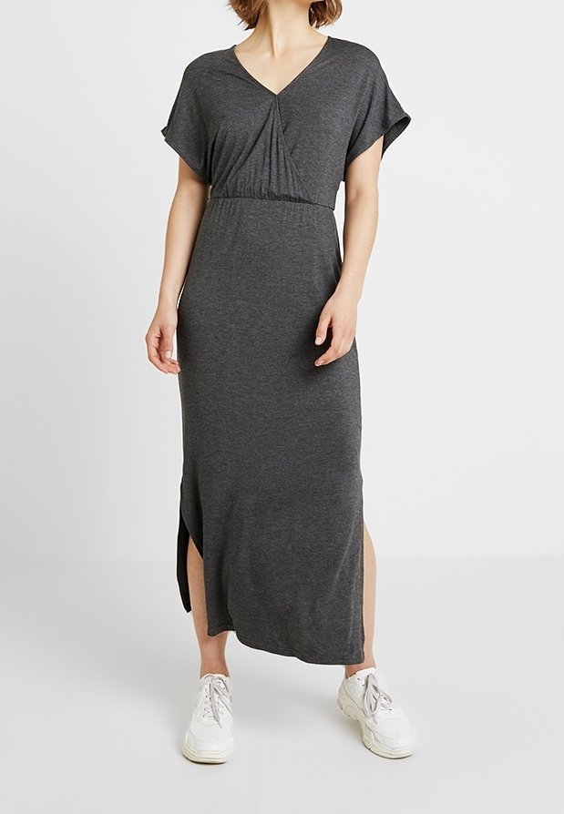 Graues Maxikleid mit V-Ausschnitt und kurzen Ärmeln. Ausgestattet mit gerafftem Detail in der Taille und seitlichen Schlitzen. Kombiniert mit weißen Sneakers.