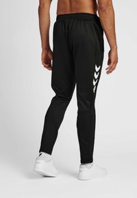 Sorte atletiske joggere med slim fit, der har elastisk talje, sidelommer og hvide chevron-accents på venstre ben.
