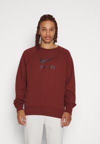 Maroon Nike sweatshirt med en svart logotyp och "AIR" tryckt i svart. Har rund hals, långa ärmar och ribbade muddar.