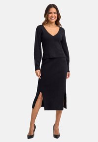 Zwart gebreid twee-delig outfit met een aansluitend langemouwen top met V-hals en een rok van gemiddelde lengte met zijspleten. Soepele textuur.
