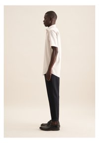 Maglietta a maniche corte a righe di un leggero beige abbinata a pantaloni neri a sigaretta e scarpe nere, che mettono in evidenza una vestibilità slim e linee pulite.