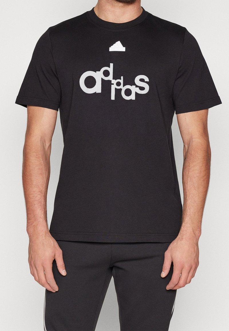 Svart bomull t-shirt med en stor grå "adidas" logotypdesign. Korta ärmar och rundad halsringning, med en liten vit logotyp på bröstet.