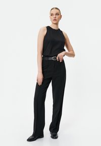 Top nero senza maniche con scollatura testurizzata, abbinato a pantaloni neri a vita alta e una cintura abbinata. Scarpe nere completano l'outfit.
