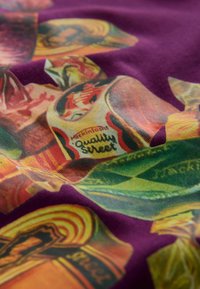 Bunte Stoffe mit Süßigkeitenmotiven, hauptsächlich in Gelb und Grün auf einem lila Hintergrund. Bemerkenswerte Details sind das „Quality Street“-Branding.