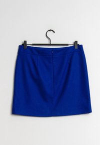 Jupe mini bleue avec détail de couture devant suspendue à un cintre noir sur fond blanc.