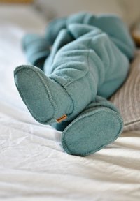 Niebieskie wełniane buciki z zaokrąglonymi noskami, miękką fakturą i przeszywanymi krawędziami. Po bokach widoczna jest mała metka z napisem "milkKINE".