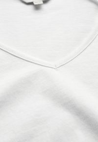 Hvid bomulds t-shirt med v-hals design, der har en blød tekstur og diskret syninger langs halsudskæringen. Ingen synlige mønstre eller accenter.