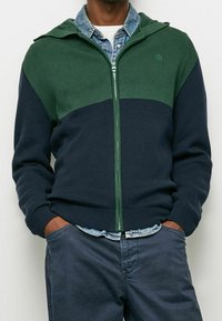 Grön och marinblå zip-up hoodie i ribbat tyg. Har en huva, kontrasterande färger och en logotypdetalj på bröstet.