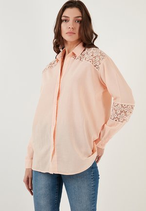Peach-colored button-up shirt with lace accents on shoulders and cuffs. Soft fabric, long sleeves, and a relaxed fit design.