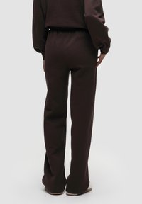 Braune, enganliegende Sweatpants aus weichem Material, mit einem elastischen Bund und geraden Beinen, von hinten gezeigt mit weißen Sneakern.