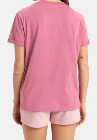 Růžové tričko s ohrnutými rukávy, měkkou texturou a volným střihem; v kombinaci se světlými růžovými šortkami vytváří sladěný ležérní vzhled.