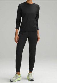 Svart atletisk set med långärm top och tapered byxor. Slät, lättviktsmaterial. Kombinerat med grå och neongröna sneakers.