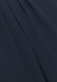 Mørkeblå stof med en glat tekstur og subtil glans. Har bløde folder, der skaber bløde draperinger i materialet.
