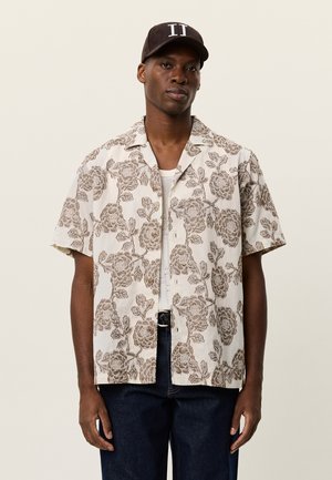 Kortærmet skjorte med knapper lavet af let stof, med en beige baggrund og mørke blomsterprint. Kombineret med marineblå denimbukser.