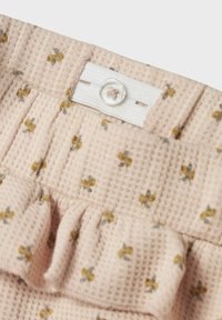 Tissu texturé rose avec un petit motif floral jaune. Présente un volant froncé en haut et une fermeture à bouton blanc sur une patte.