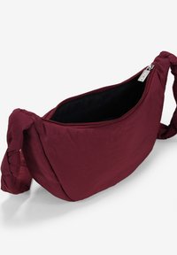 Borsa a spalla bordeaux con una texture morbida, chiusura con zip e tracolle annodate. Interno foderato senza motivi visibili o dettagli in metallo.