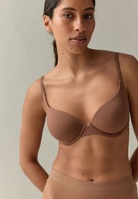 Pruun pehme rinnahoidja reguleeritavate rihmadega ja ühtlase tekstuuriga, esikinnitusega ja minimalistliku disainiga. Kombineeritud sobivate pükstega.