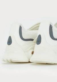 Bílé sportovní boty s šedými akcenty, síťovinový materiál na patě, zaoblený design, s výrazným logem po straně.