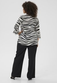 Bluza cu dungi de zebre alb-negru cu mâneci evazate, asortată cu pantaloni negri largi și pantofi cu toc negri, văzută din spate.