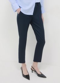 Pantalon marine ajusté à coupe slim et texture lisse, associé à des escarpins noirs à bride arrière pointus. Design classique pour un port polyvalent.