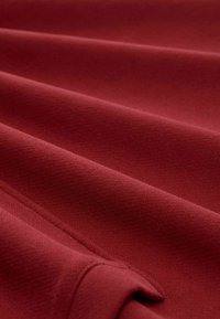 Czerwony materiał o miękkiej teksturze z delikatnymi żłobieniami i fałdami, prezentujący głęboki, jednolity kolor i gładką powierzchnię.