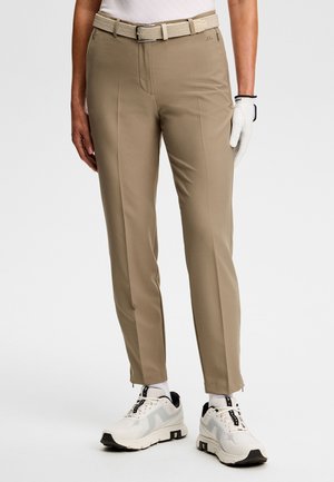 Beżowe spodnie do golfa o zwężanym kroju, z teksturowanym paskiem, przednimi kieszeniami i suwakami przy kostkach. W połączeniu z białymi butami sportowymi.