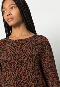 Camisola de padrão animal castanho com decote redondo e mangas longas, apresentando um tecido texturizado em um ajuste solto, acentuado por manchas pretas.