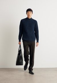 Maglione a coste in navy, pantaloni neri e borsa a tracolla nera. Il modello indossa un berretto nero. Design alla moda, aderente con texture lisce.