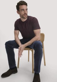Bordeaux T-shirt, blauwe corduroy broek, donkerbruine schoenen, zittend op een houten stoel. Eenvoudig ontwerp met een gladde textuur.