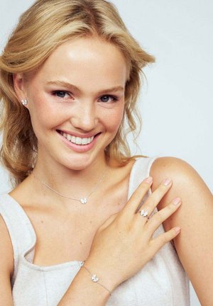 Silverfjärilssmyckeset som inkluderar örhängen, ett halsband och en ring. Har intrikata detaljer och en polerad finish på en ljus bakgrund.