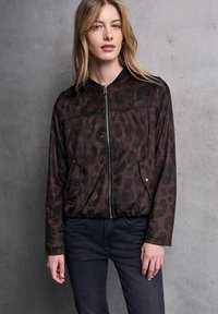 Giacca bomber con stampa leopardata marrone, dotata di zip frontale, colletto a coste e due tasche laterali, abbinata a jeans in denim scuro.