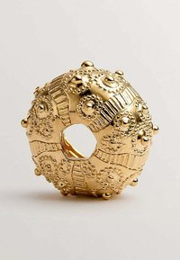 Anillo decorativo de oro con patrones en relieve, acentos texturizados y un corte circular central. Superficie lisa con un intrincado detalle.