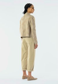 Beige mønstrete genser med høy krage, sammen med lyse khaki bukser rullet opp ved anklene og skinnende beige leiligheter.