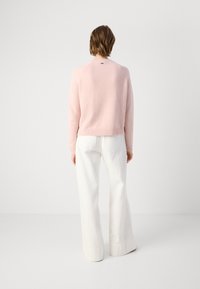 Pull en laine rose tricoté avec un ourlet côtelé, en fil texturé ; associé à un pantalon large blanc avec poches arrière et finitions soignées.