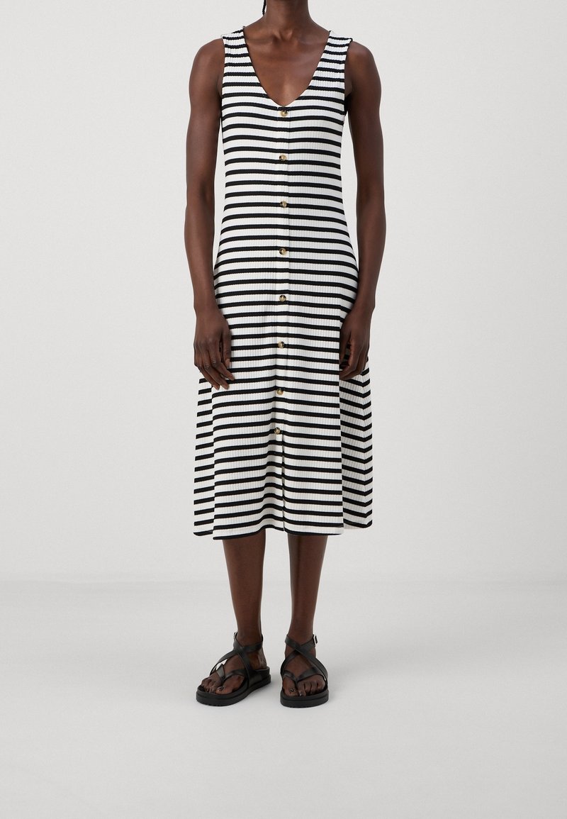 Robe midi rayée en noir et blanc, tissu côtelé, encolure en V, boutons sur le devant, associée à des sandales noires.