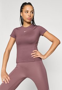 Tettpassende treningsgenser i mauve, laget av elastisk materiale. Har rund hals, korte ermer og en liten hvit logo på brystet.