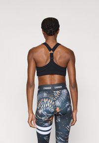 Black sports bra with racerback design and adjustable straps; high-waisted leggings with colorful abstract patterns and contrast waistband.