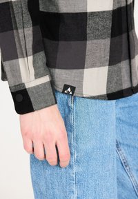 Zwarte en grijze plaid flanellen shirt met knoopmanchetten, zwarte accenten en een merklabel aan de zoom, gecombineerd met lichtblauwe denim jeans.