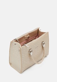 Sac fourre-tout beige avec motif en relief, matériel en argent double ton, et anses tressées texturées. S'ouvre sur un intérieur tapissé de rose avec fermeture zip.