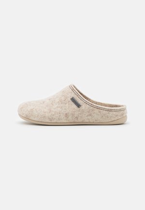 Pantoufle en feutre beige avec une texture douce, un bout arrondi et un dos bas. Elle dispose d'une bordure contrastante et d'une petite étiquette sur le côté.
