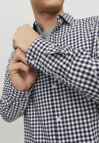 Camisa de cuadros azul marino y blanca con mangas largas, material de algodón y cuello clásico; cuenta con botones blancos en la parte delantera.