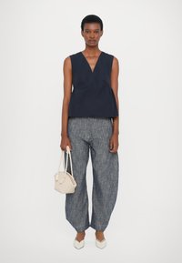 Top senza maniche blu navy con scollatura a V e dettagli plissettati, abbinato a pantaloni blu larghi e di tessuto leggero, ballerine bianche a punta e una borsa chiara.