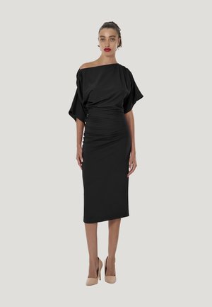Schwarzes schulterfreies Kleid mit kurzen, voluminösen Ärmeln und gerafften Details an der Taille, kombiniert mit nudefarbenen High-Heel-Schuhen.